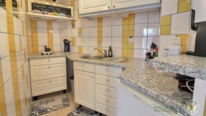 A kitchen with white cabinets, a granite countertop, a sink, and a chalkboard sign. - Gîte la Crabière, 900m de la Mer, Animaux de Compagnie Bienvenue (SAINT CAST le guildo)