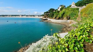 A coastal scene with a beach, a large house on a cliff, and calm sea. - Gîte la Crabière, 900m de la Mer, Animaux de Compagnie Bienvenue (SAINT CAST le guildo)