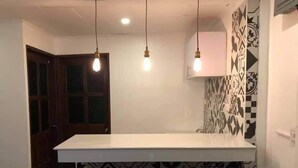 Een keuken met een wit aanrecht, hangende lampen en patroon betegelde vloeren.