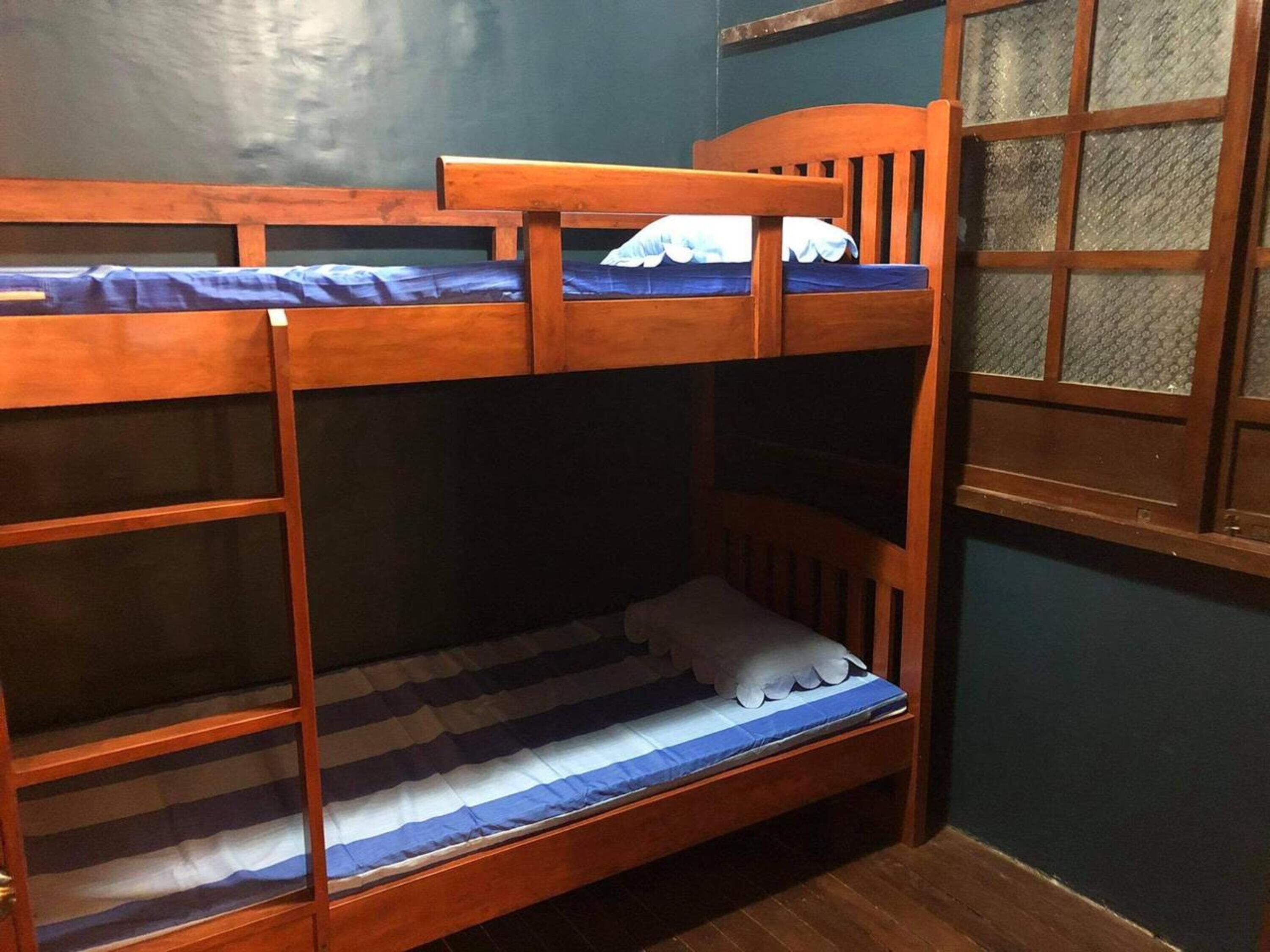 Una cama literera con estructura de madera y una ventana con persiana estampada.