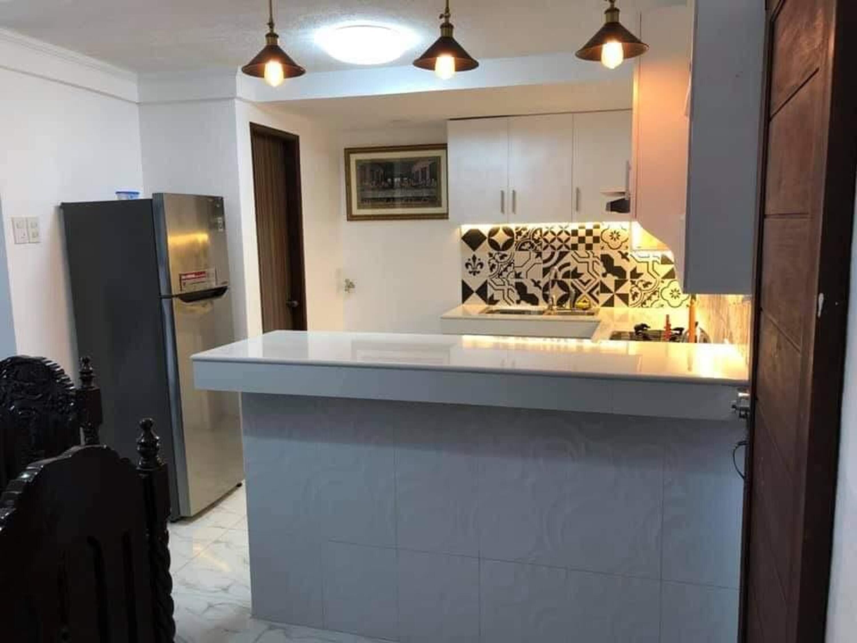 Una cocina con mostrador blanco, salpicadero con estampado blanco y negro e iluminación colgante.