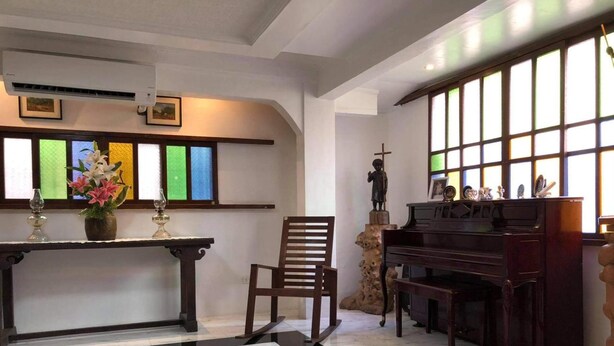 Een kamer met een piano, een beeld, een stoel, een tafel met bloemen en een glas-in-loodraam.