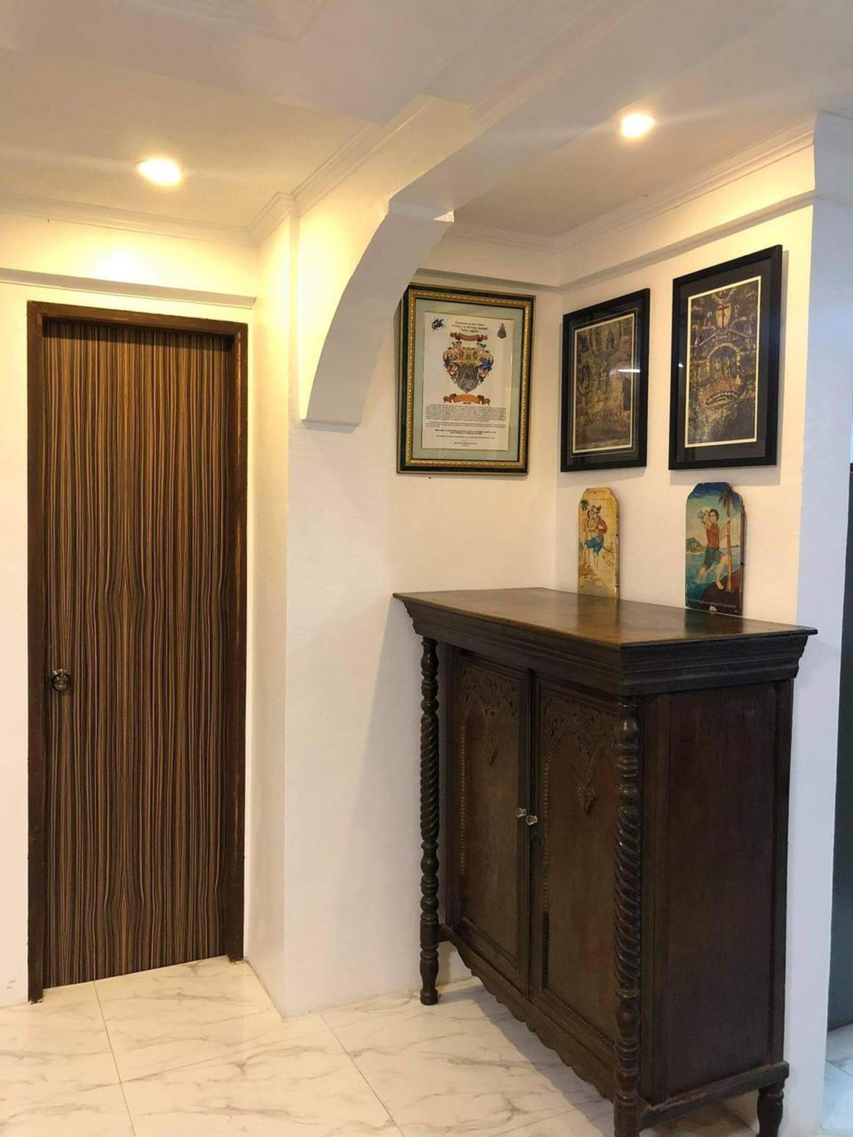 Um corredor com uma porta de madeira, um armário escuro de madeira e três obras de arte emolduradas na parede.