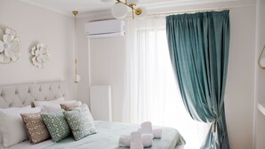 Una cama bien hecha con almohadas, un ventanal con cortinas y un aire acondicionado instalado en la pared.