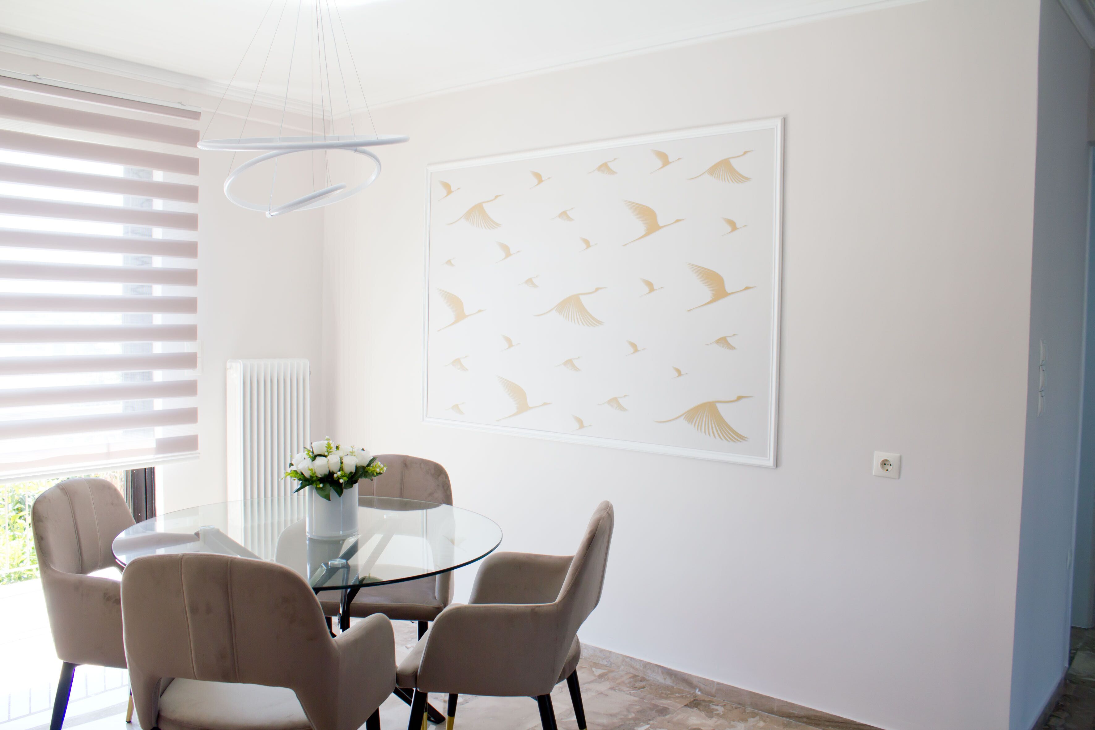 Ein Essbereich mit einem Glastisch, vier Stühlen, einer Vase mit Blumen und einem Bilderrahmen mit einer Vogelmotive an der Wand.