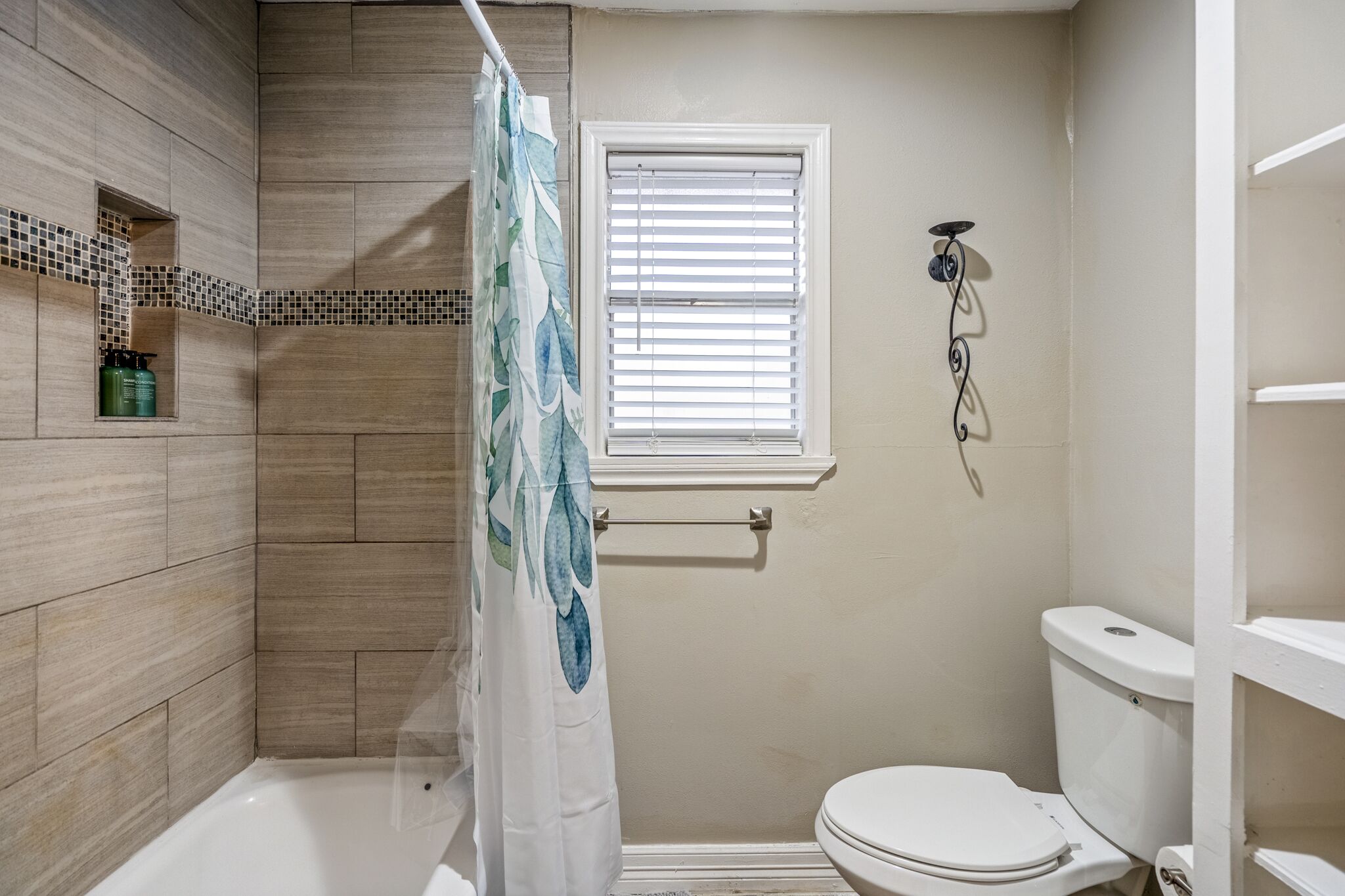 Un baño con ducha, inodoro y ventana con persianas.