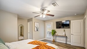 A bedroom with a bed, a ceiling fan, a TV, a door, and a window. - Modern Home with Private Pool, Minutes to NRG & Med Center (Houston)