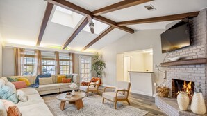 A cozy living room with a sectional sofa, a fireplace, and a television mounted on the wall. - Modern Home with Private Pool, Minutes to NRG & Med Center (Houston)