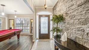 A pool table in a spacious room with a stone wall and a door with a decorative glass panel. - Modern Home with Private Pool, Minutes to NRG & Med Center (Houston)