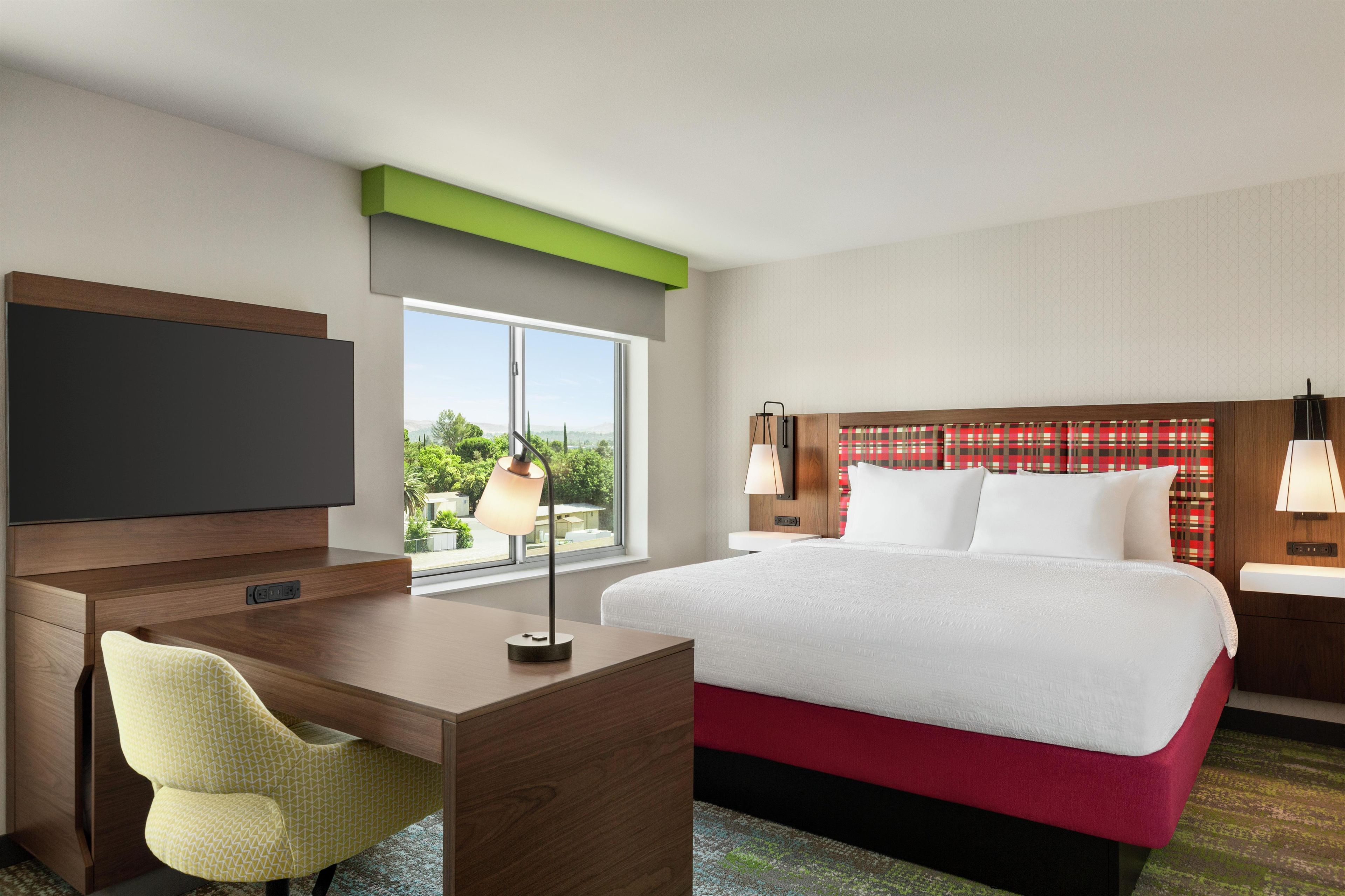 A hotel room with a bed, a desk, a chair, a television, and a window with a view.