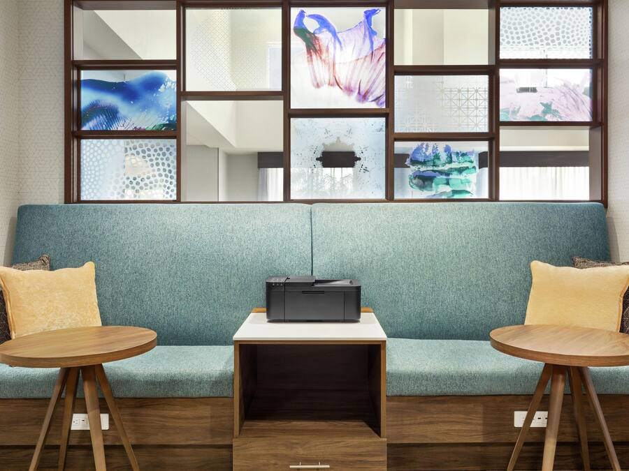 A modern room with a teal sofa, two wooden side tables, and a black printer.