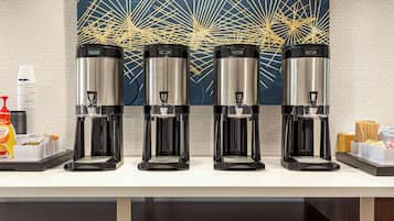 A coffee station with four coffee makers and a wall art piece.