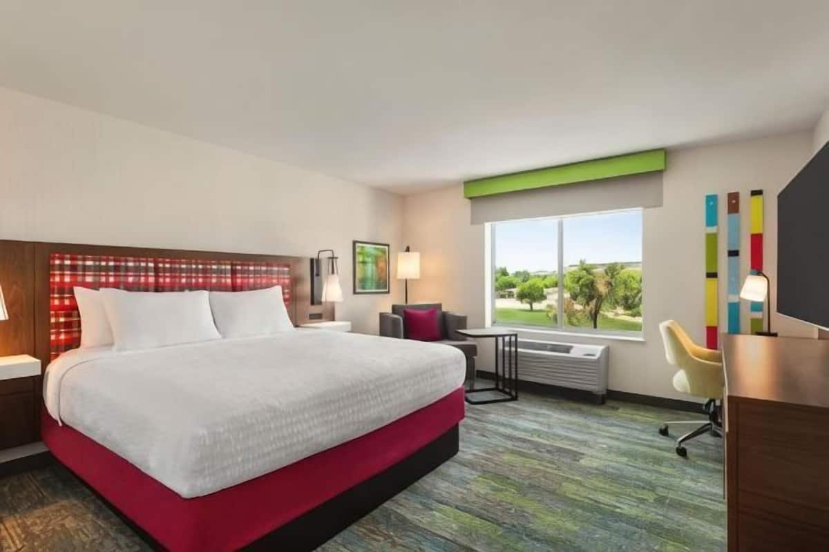 A hotel room with a bed, a desk, a chair, a window with a view, and a wall-mounted TV.