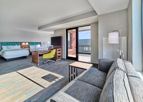 Habitación de hotel con cama, escritorio, silla, sofá y balcón con vistas.