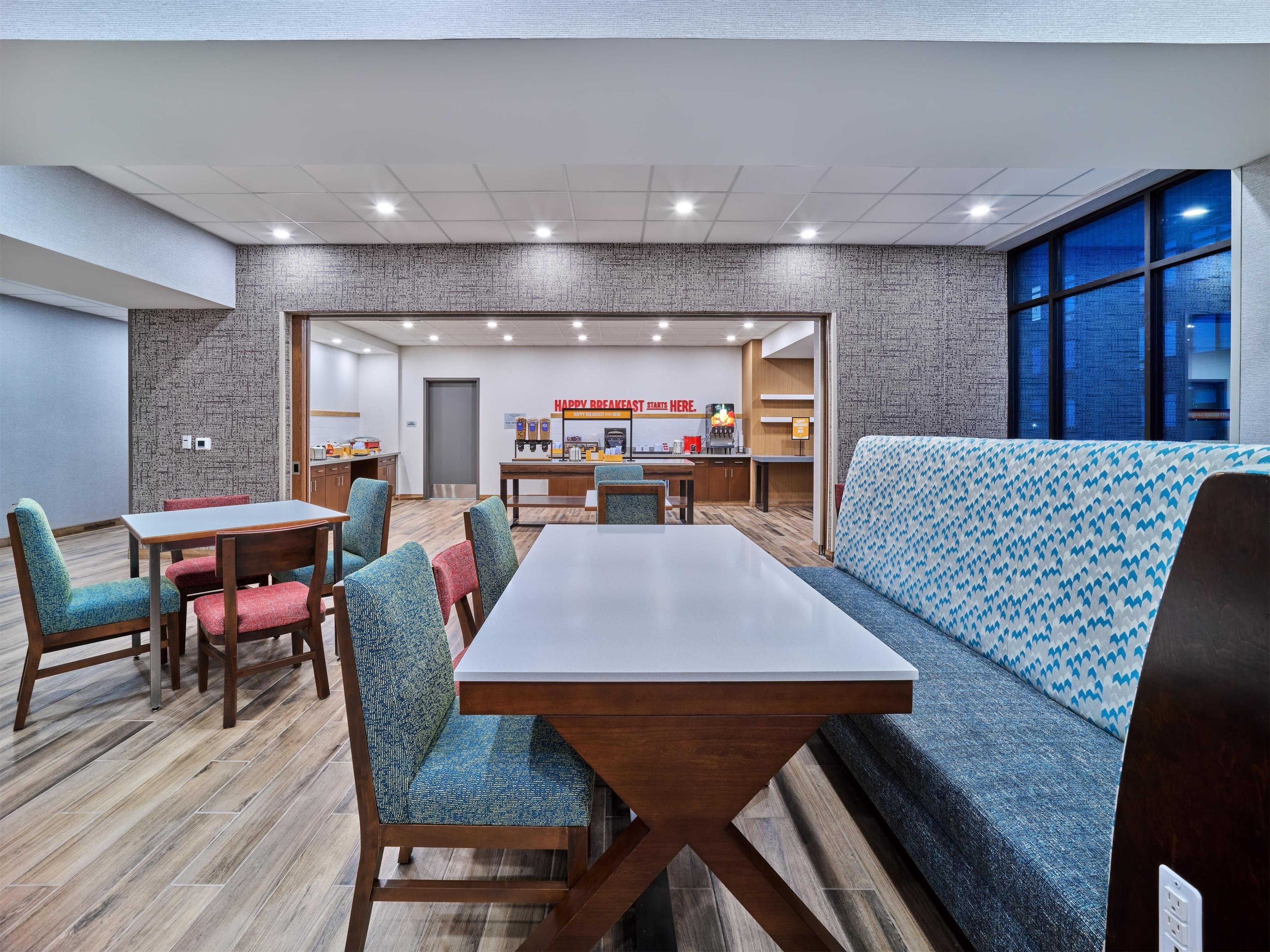 A modern hotel room with a dining area, a kitchen, and a seating area with a patterned sofa.