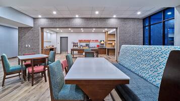 A modern hotel room with a dining area, a kitchen, and a seating area with a patterned sofa.