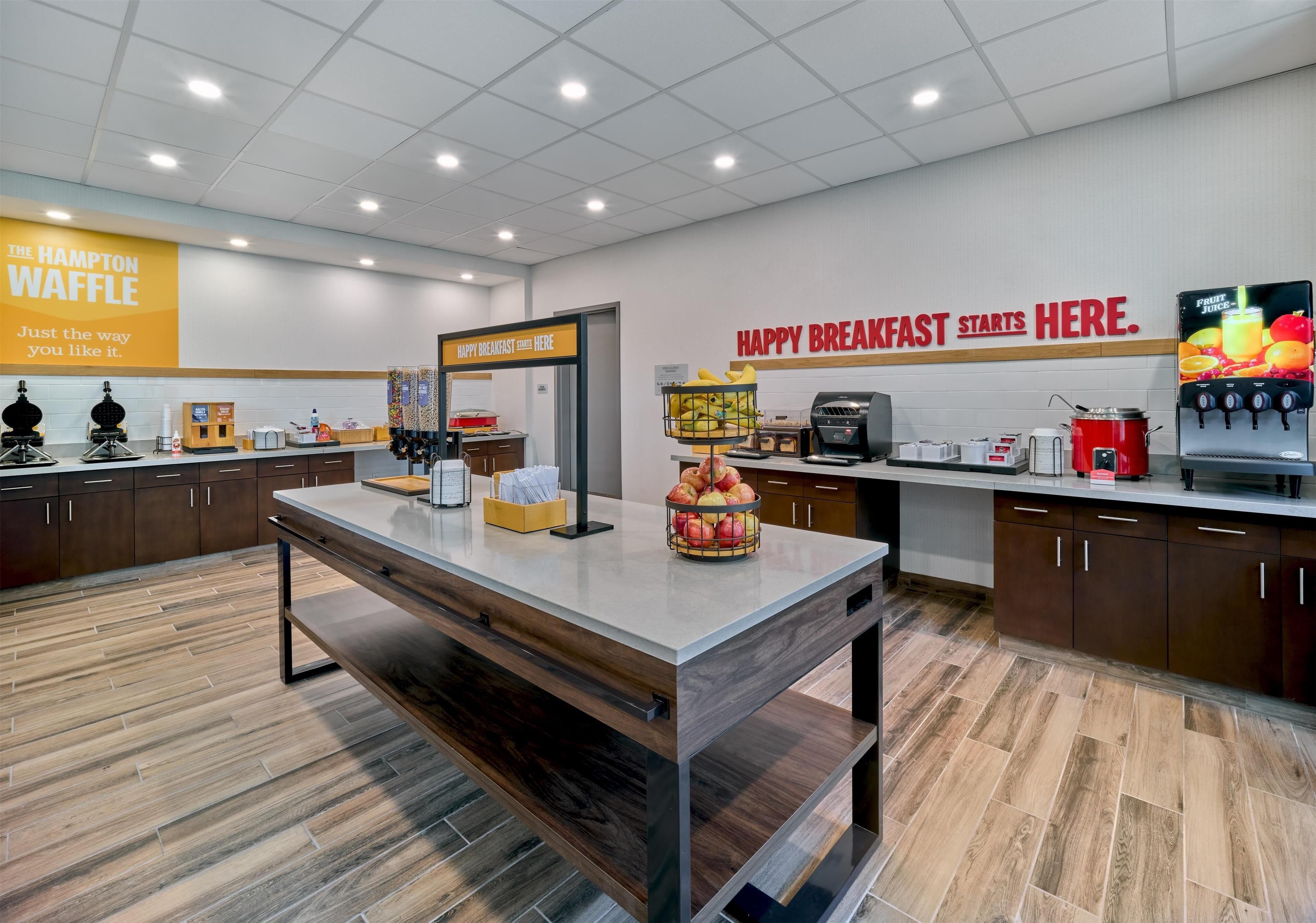 Un'area cucina moderna con una colazione bar, un cartello con la scritta The Hampton Waffle e un distributore di succo di frutta.
