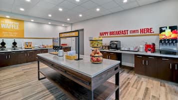 A modern kitchen area with a breakfast bar, a sign for The Hampton Waffle, and a fruit juice dispenser.