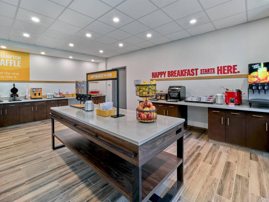 A modern kitchen area with a breakfast bar, a sign for The Hampton Waffle, and a fruit juice dispenser.
