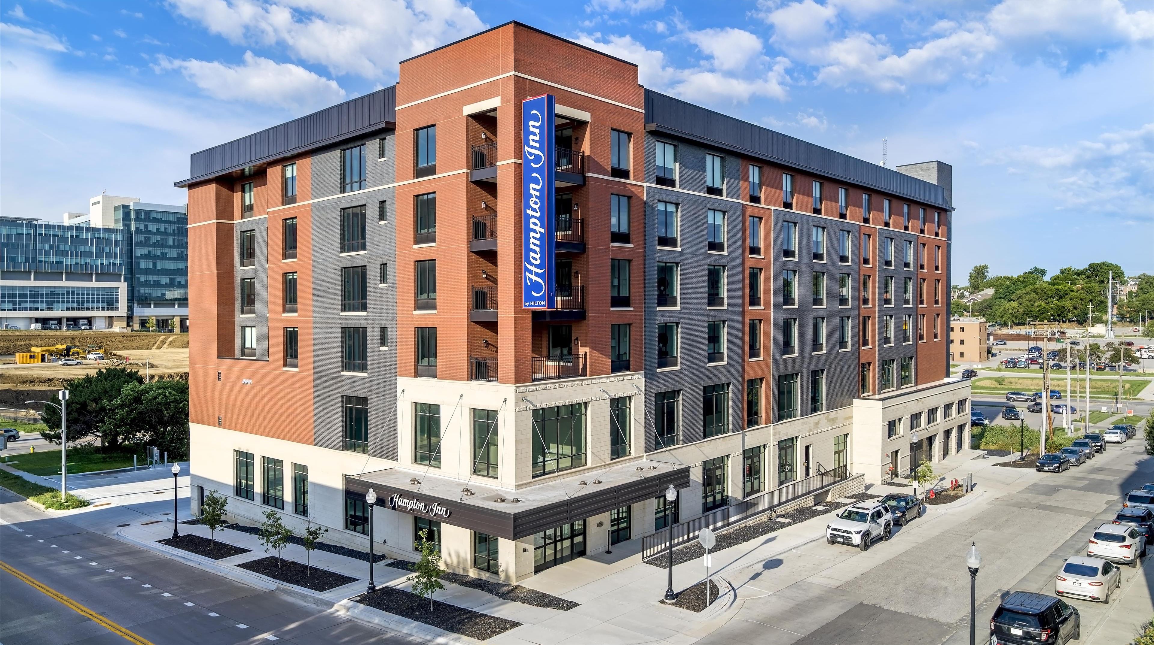 A modern hotel with a prominent Hilton sign, multiple floors, and a parking lot with several cars.