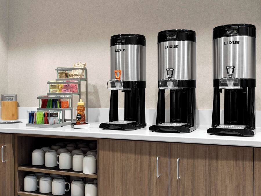 A coffee station with three black and silver Luxus coffee makers on a white countertop.