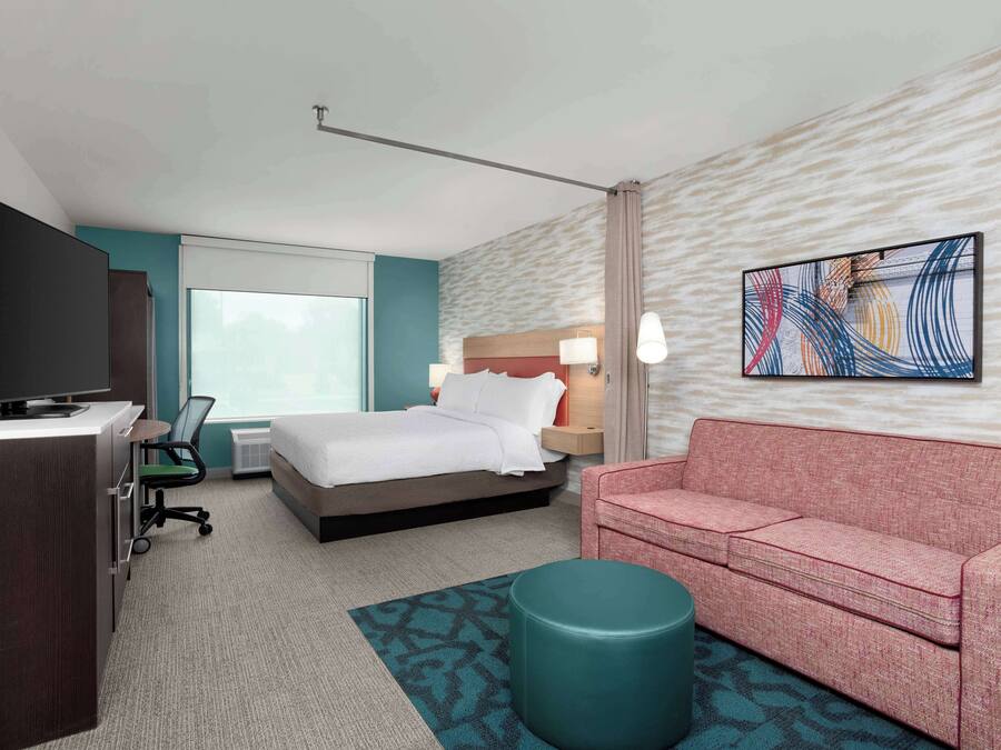 A hotel room with a bed, a desk, a television, a red sofa, and a patterned rug.