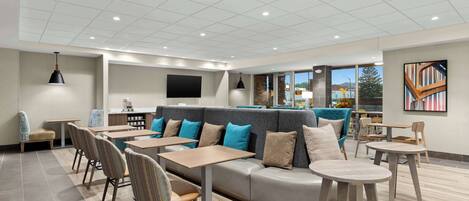A modern lounge area with a sofa, tables, chairs, and a flat-screen TV.