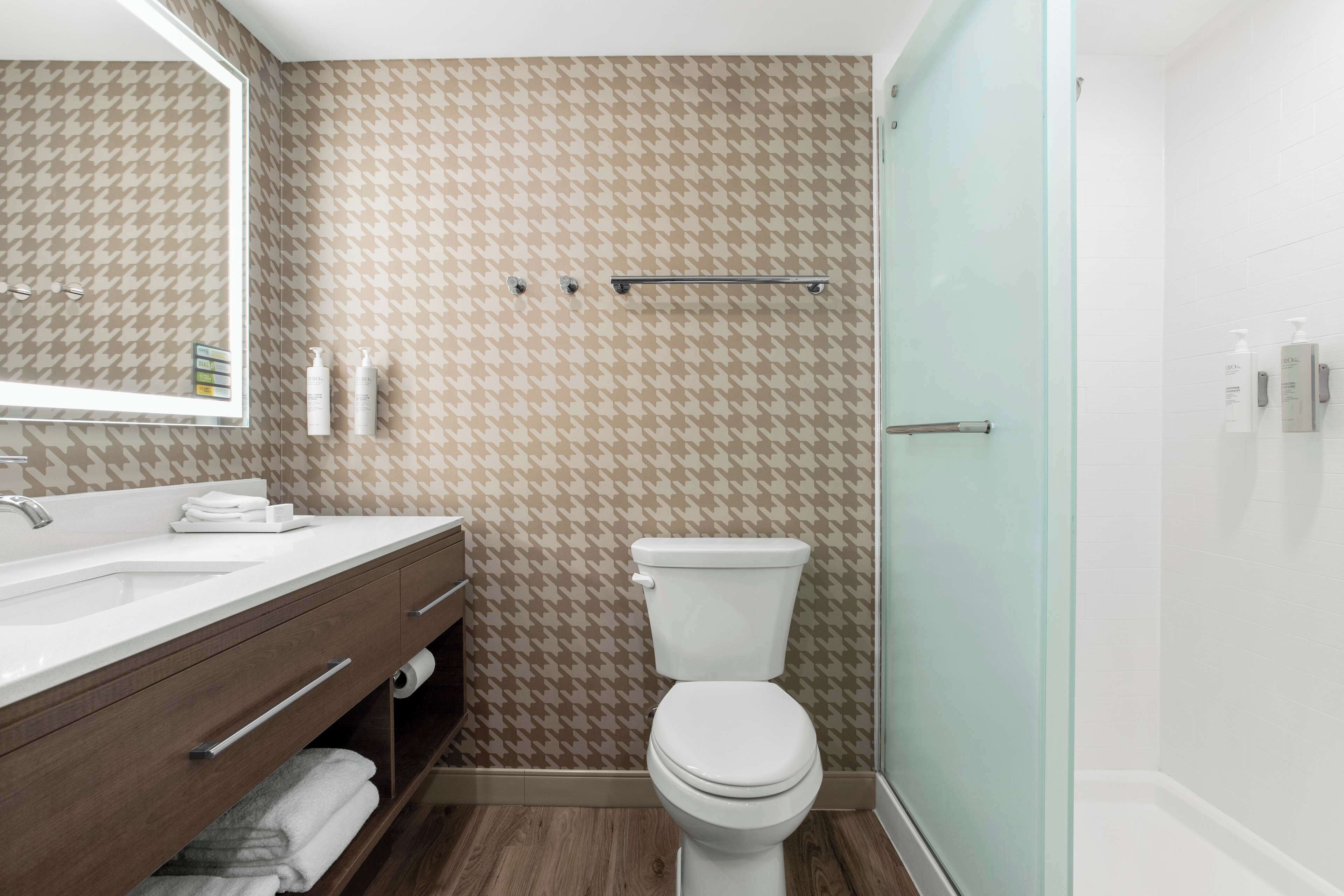 Un baño con pared de estampado pata de gallo, un lavamanos blanco, un inodoro y una cabina de ducha de vidrio.