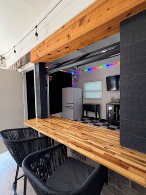 A modern kitchen with a wooden countertop, black chairs, a refrigerator, a TV, and colorful LED lights. - Bama's Best Tailgate Home (Tuscaloosa)