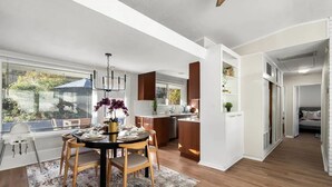 Una cocina moderna con armarios de madera, una zona de comedor con mesa y sillas redondas, y vistas al exterior a través de ventanas amplias.