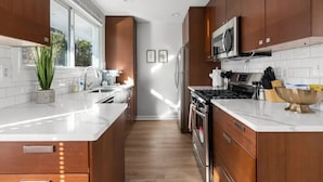 Una cocina moderna con armarios de madera, electrodomésticos de acero inoxidable y un amplio ventanal que proporciona luz natural.