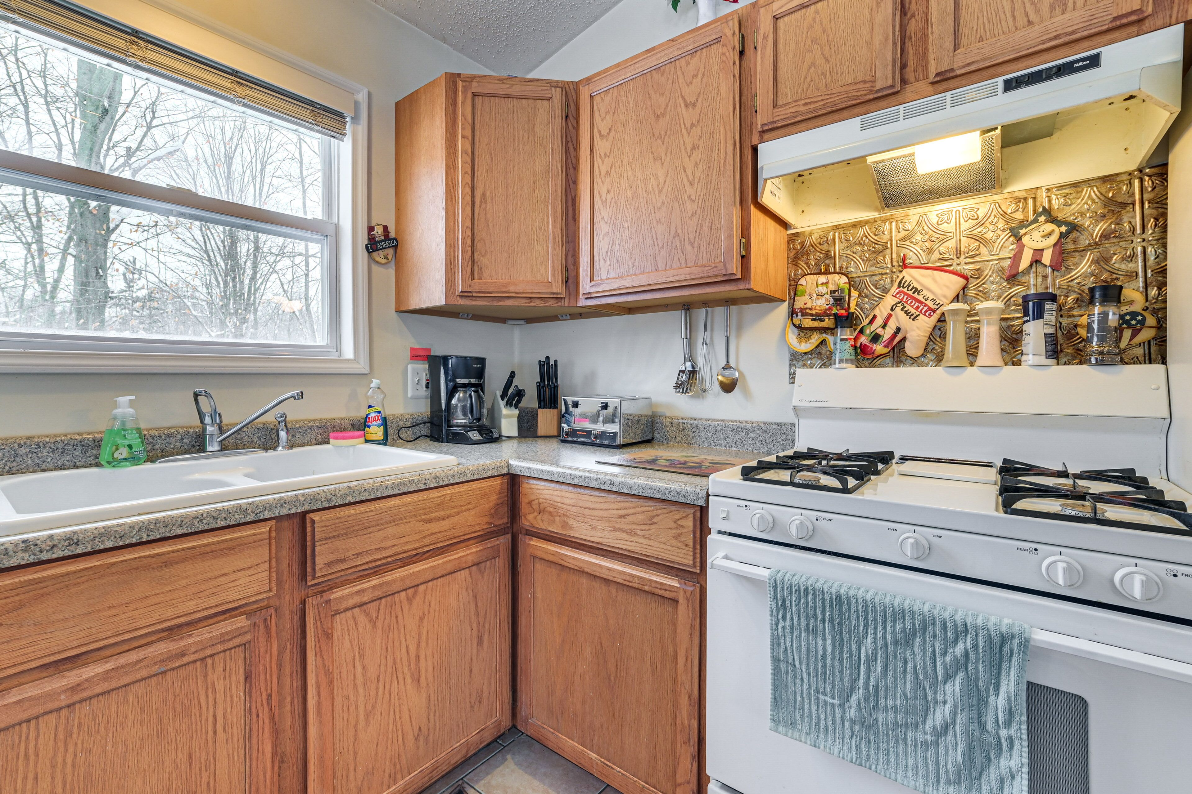 A kitchen with wooden cabinets, a sink, a stove, and various kitchen items.
