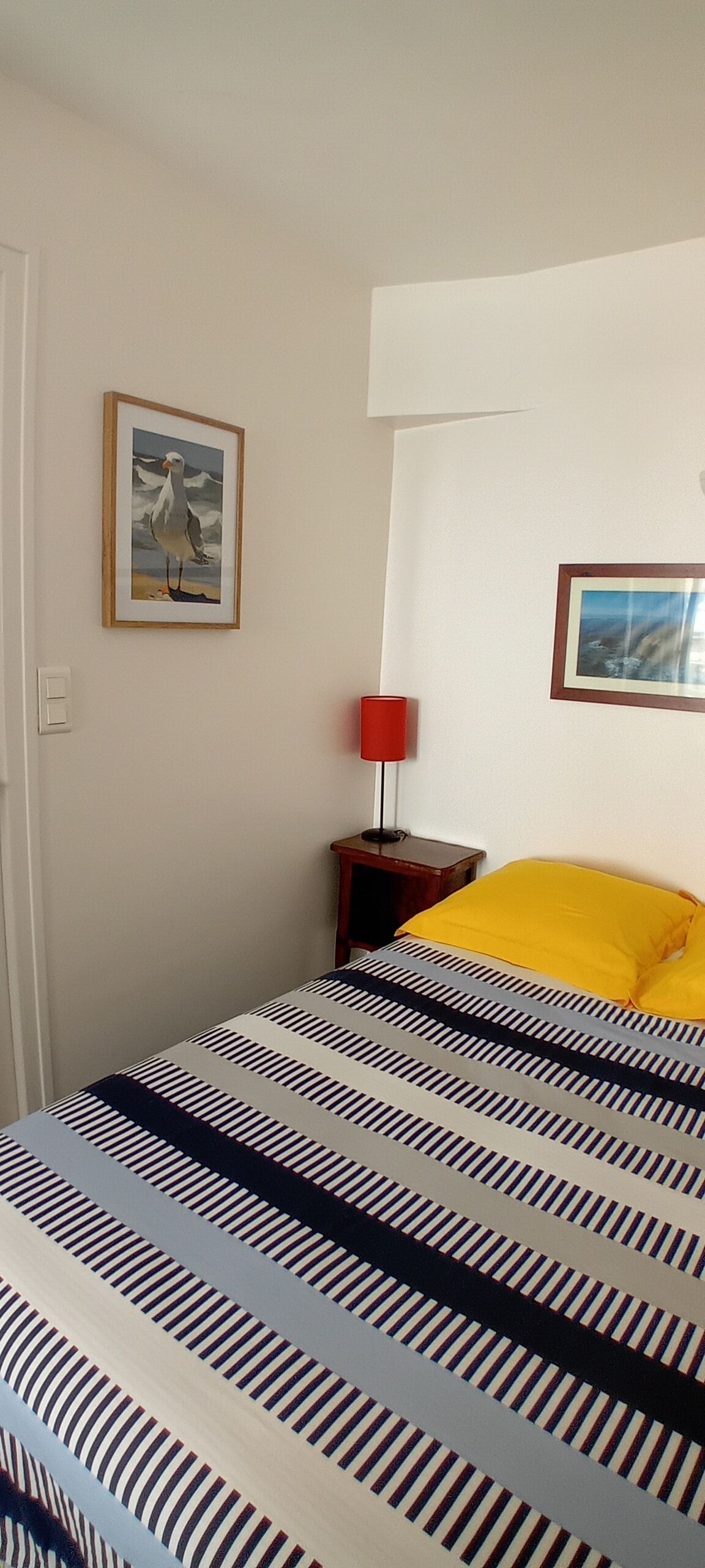A bed with striped bedding, a red lamp, and two framed pictures on the wall.