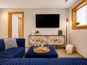 A living room with a blue sofa, a coffee table with snacks, a flat-screen TV, and a decorative cabinet. - Modern spacious 4 bedroom retreat with 3 en-suites and all year round hot tub (Galena)