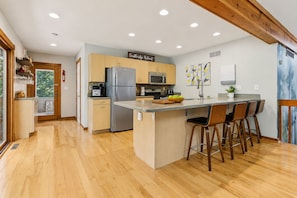 A modern kitchen with wooden cabinets, a stainless steel refrigerator, a microwave, and a large island with bar stools.