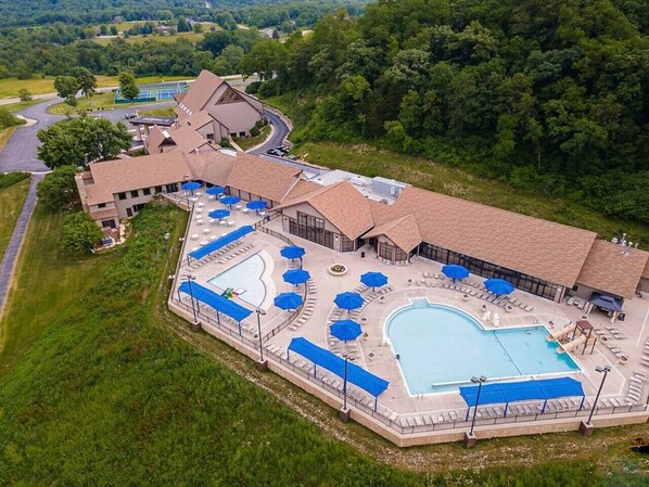An aerial view of a resort with a large swimming pool, multiple lounge areas with umbrellas, and a building with a curved roof. - Modern spacious 4 bedroom retreat with 3 en-suites and all year round hot tub (Galena)