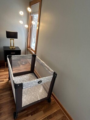 A room with a baby playpen, a bedside table with a lamp, and a large mirror. - Modern spacious 4 bedroom retreat with 3 en-suites and all year round hot tub (Galena)