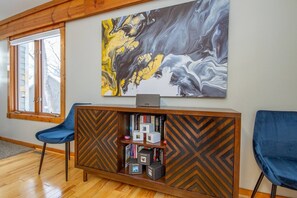 A modern room with a wooden bookshelf, two blue chairs, and a large abstract painting on the wall. - Modern spacious 4 bedroom retreat with 3 en-suites and all year round hot tub (Galena)