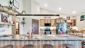 A modern kitchen with a marble countertop, wooden cabinets, and a central island with stools.