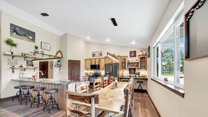 A spacious kitchen with a central island, wooden bar stools, and a dining area with a large wooden table.