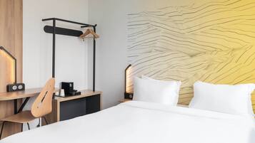 A hotel room with a bed, a desk with a chair, a coat rack, and a wall with a textured design.