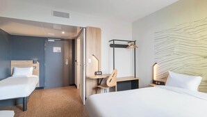 A hotel room with a large bed, two smaller beds, a desk, a chair, and a wall-mounted coat rack. - B&B HOTEL Villefranche-sur-Saône Sud (Villefranche-sur-Saône)