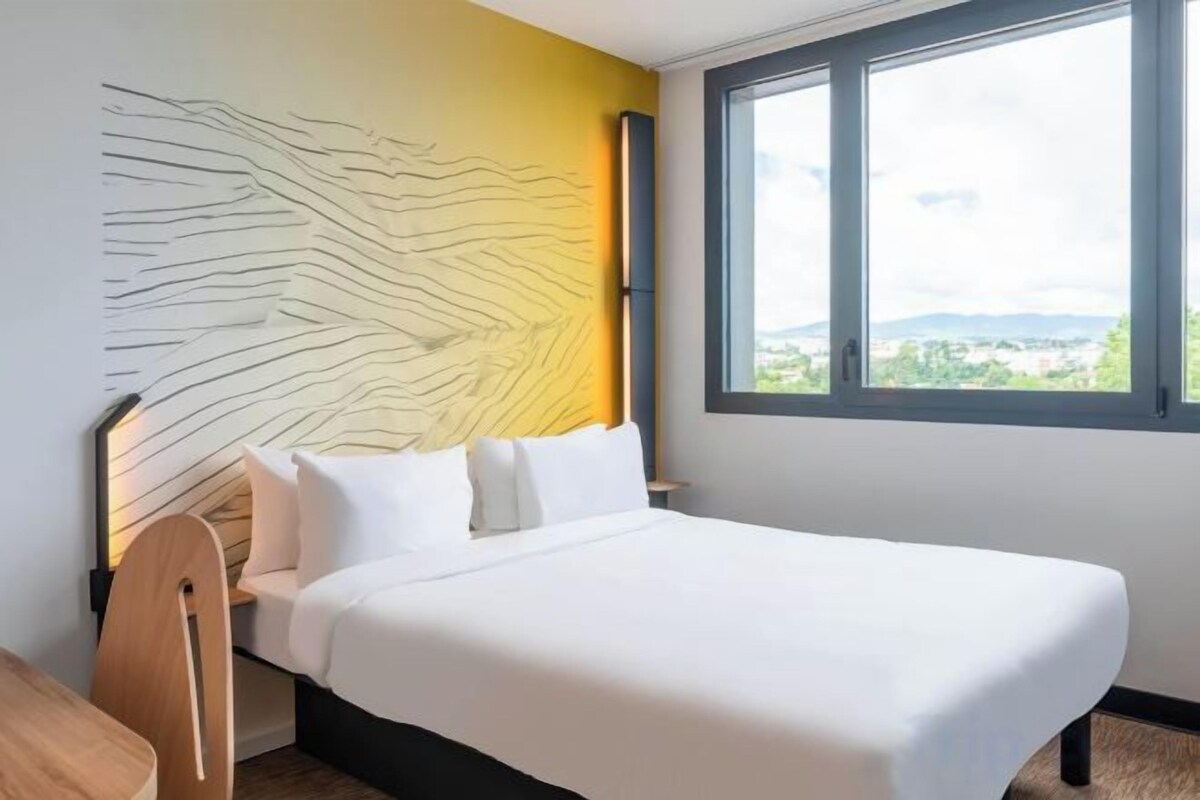 Habitación de hotel con una cama, vistas por una ventana y una obra de arte en la pared.