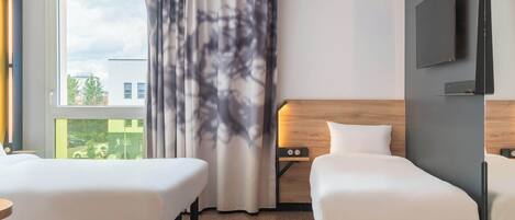A hotel room with two beds, a large window with curtains, a flat-screen TV mounted on the wall, and a wooden headboard.