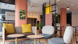A modern lounge area with a sofa, two round tables, and a grey armchair. - B&B HOTEL Villefranche-sur-Saône Sud (Villefranche-sur-Saône)