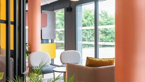 A modern interior with a seating area, large windows, and a view of greenery outside. - B&B HOTEL Villefranche-sur-Saône Sud (Villefranche-sur-Saône)