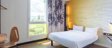 Quarto de hotel com uma cama grande, uma escrivaninha com cadeira, janela com cortinas e parede com design texturizado.
