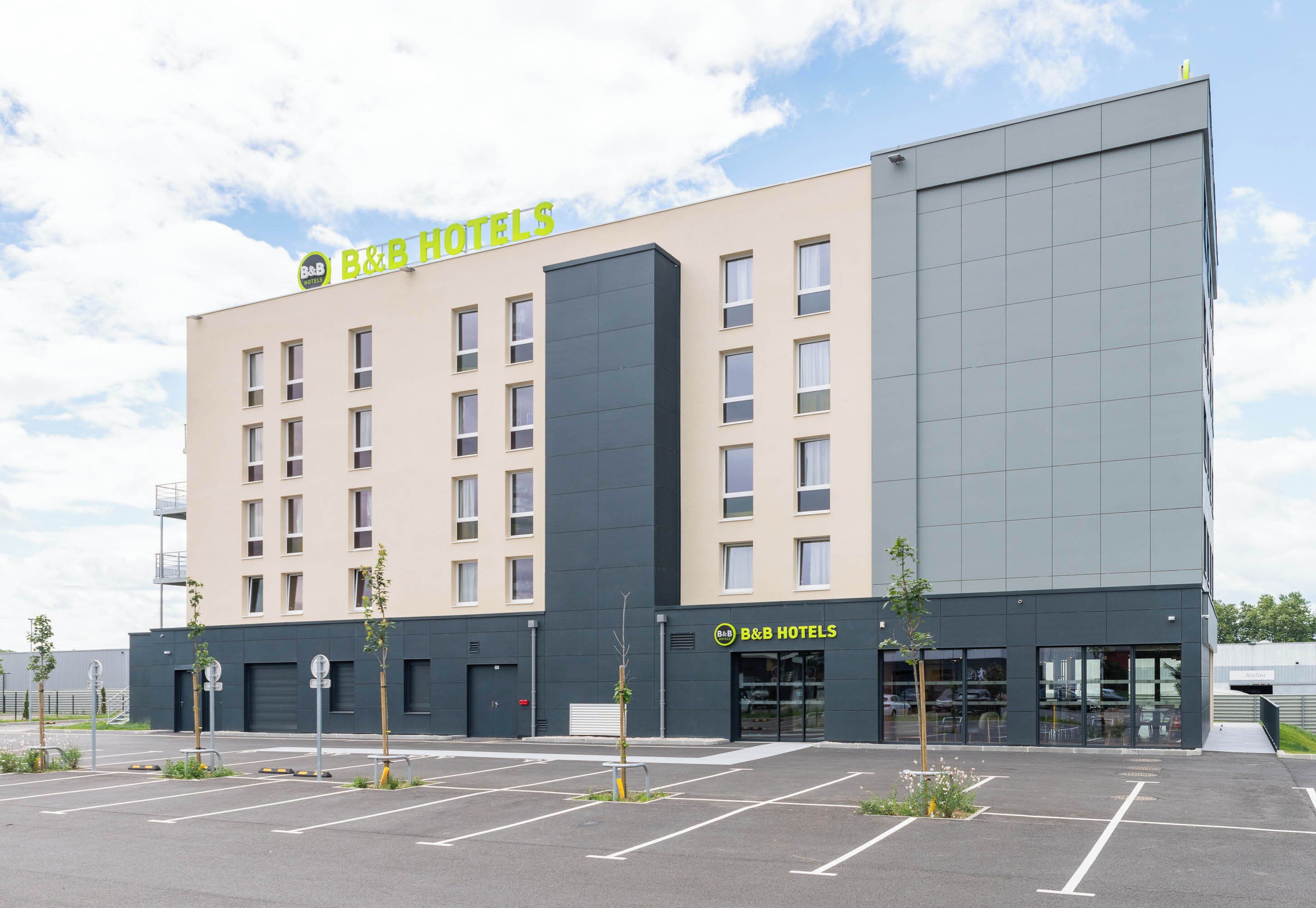 Un hotel B&B con fachada moderna, varios ventanales y un estacionamiento con espacios delimitados.