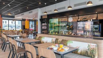 Un café moderno con mesas y sillas de madera, un amplio ventanal con vistas al exterior y una barra con productos alimenticios.