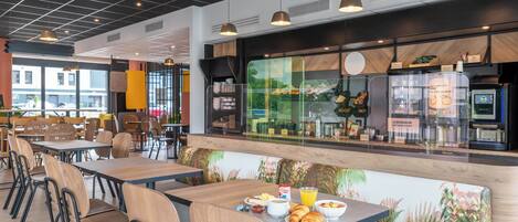 Un café moderno con mesas y sillas de madera, un amplio ventanal con vistas al exterior y una barra con productos alimenticios.